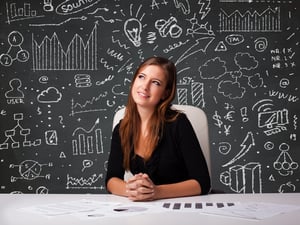 Pretty young businesswoman sitting at desk with business scheme and icons